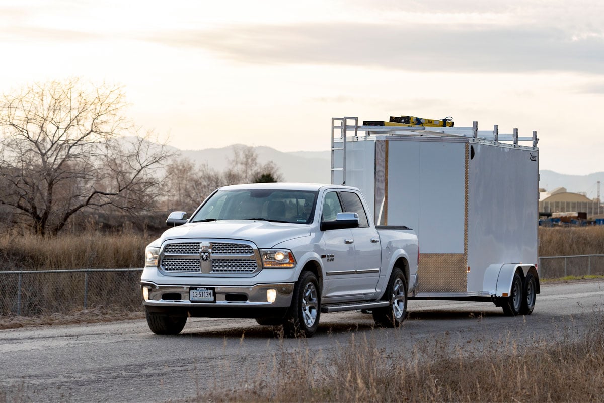 Front View Of White Truck Hauling White Xpress Enclosed Ultimate Contractor Trailer Going Through Construction Site