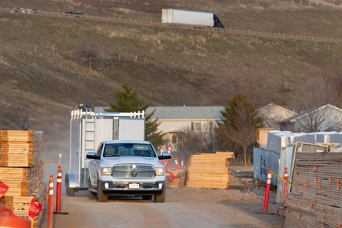 Front View Of White Truck Hauling White Xpress Enclosed Ultimate Contractor Trailer Going Through Site