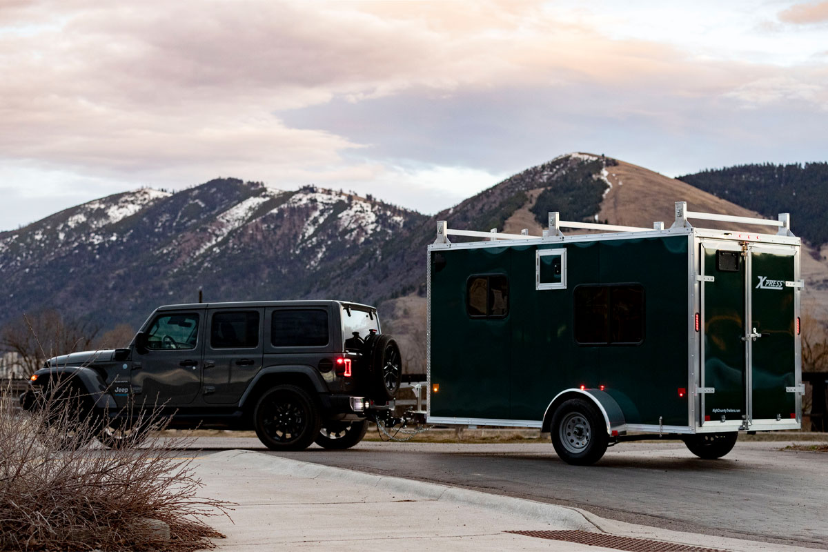 Side View Of Gray Jeep Hauling Enclosed Cargo 5/6 Wide Trailer Behind Mountains